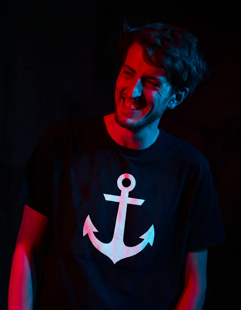 Brighten this dark portrait photo significantly. Lift the shadows, increase exposure and brightness, bring out details in the dark areas while keeping the colorful red and blue lighting mood. The person and their shirt logo should be clearly visible.